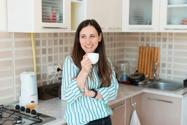 Joven mujer alegre en informal de pie en la cocina y beber taza de café — Foto de Stock