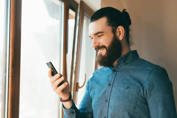 Photo of cheerful bearded hipster man in casual using smartphone and smiling — Stock Photo, Image