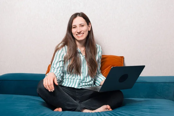 Foto de jovem mulher alegre em casual sentado no sofá e segurando laptop — Fotografia de Stock