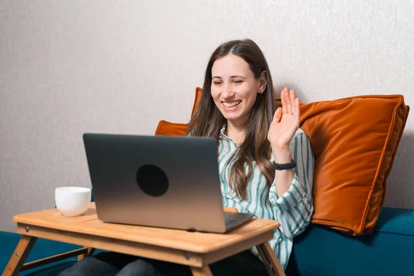 Foto einer lächelnden Frau vor dem Laptop, die auf dem Sofa sitzt und ein Online-Treffen hat — Stockfoto