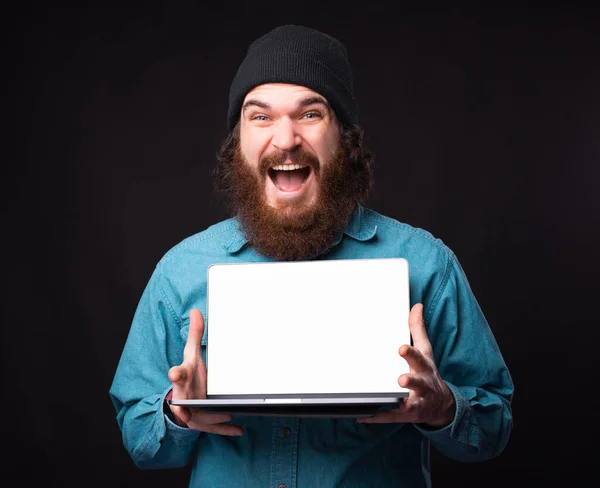 Joyeux homme étonné avec barbe montrant écran vide blanc sur ordinateur portable. — Photo
