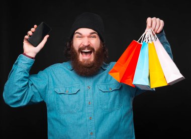 Akıllı telefon ve küçük renkli alışveriş torbaları tutan harika sakallı hippi.