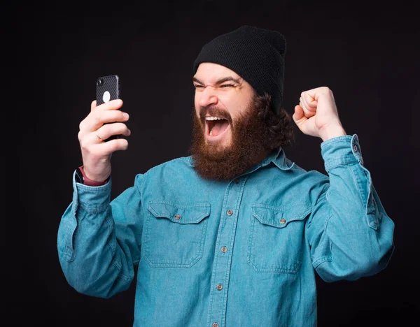 Hombre barbudo asombrado mirando el teléfono inteligente gritando y celebrando — Foto de Stock