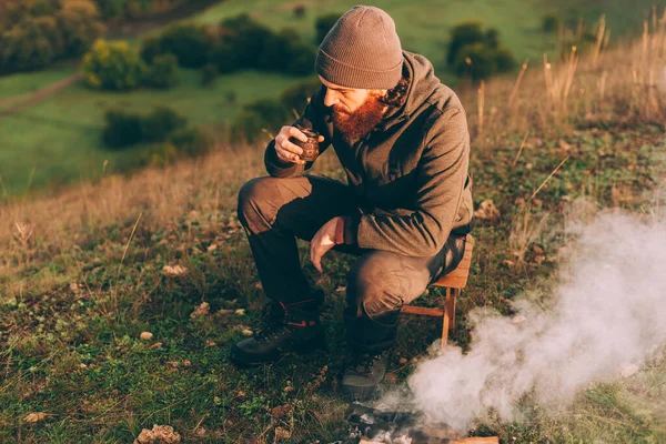 Photo of bearded man drinking coffee in the morning near camp fire — Stock Photo, Image