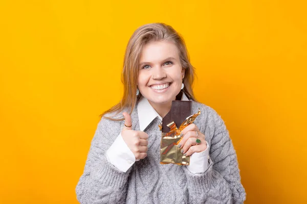 Foto de mujer joven en la barra de retención casual de chocolate negro y mostrando el pulgar hacia arriba — Foto de Stock