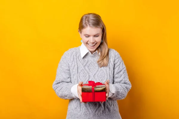 Erstaunt hält ein junges Mädchen ein Geschenk in der Hand, das sie auf gelbem Hintergrund bekommen hat. — Stockfoto