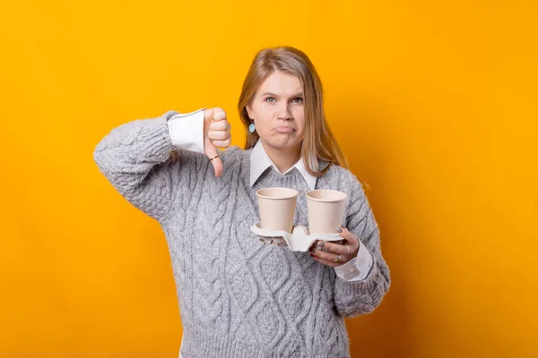Bad coffee. Young woman showing thumb down and holding cups of coffee, bad taste