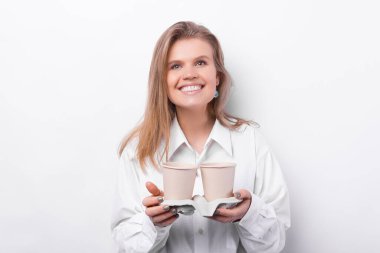 Cheerful young woman in white shirt holding two cups of coffee to take away