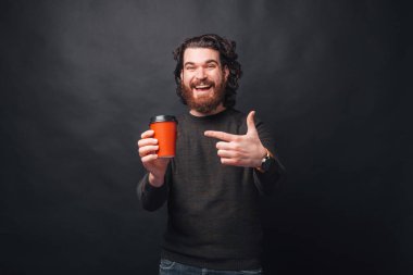 Happy man with beard in casual pointing at red cup of coffee to take away