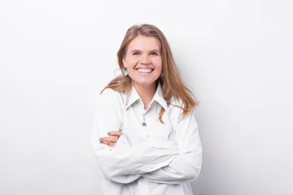 Retrato de una joven hermosa mujer en camisa blanca sonriendo y de pie con los brazos cruzados sobre fondo blanco — Foto de Stock