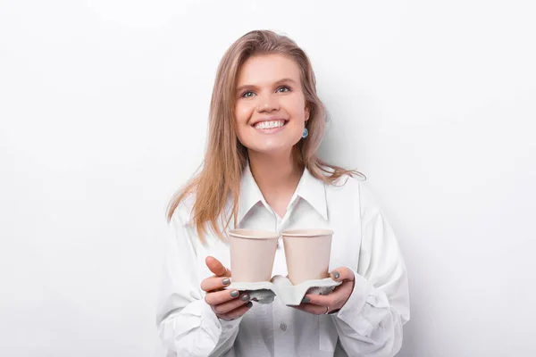 Весела молода жінка в білій сорочці тримає дві чашки кави, щоб забрати — стокове фото