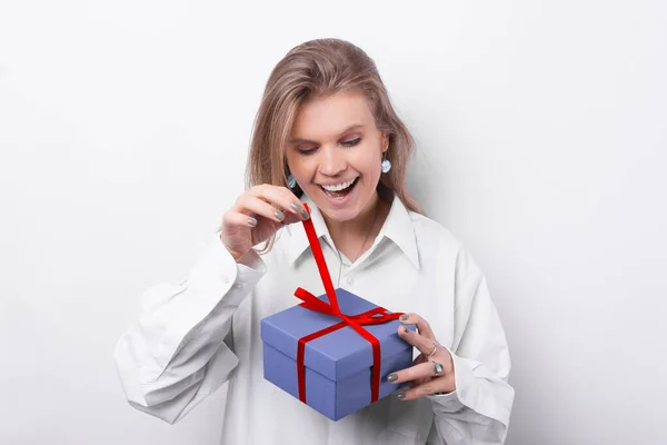 Foto de mujer joven sorprendida en camisa blanca abriendo una caja de regalo sobre fondo blanco —  Fotos de Stock