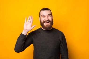 Photo of joyful happy bearded hipster man making hello gesture over yellow background