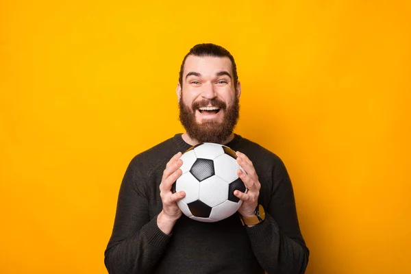 Retrato de homem barbudo feliz segurando bola de futebol sobre fundo amarelo — Fotografia de Stock
