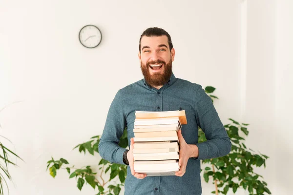 Portrait of amazed office worker man holding a bunch of books