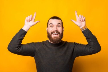 Portrait of amazed bearded hipster man pointing up at some product