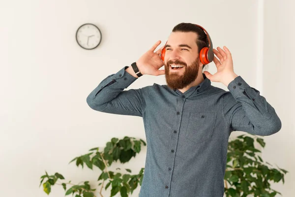 Joyeux jeune homme barbu décontracté au bureau écoutant de la musique à des écouteurs sans fil — Photo