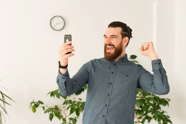 Homme barbu incroyable dans le bureau en regardant smartphone et célébrer — Photo