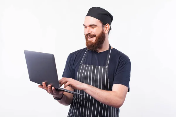 Fröhlich Koch Mann in Uniform mit Laptop über weißem Hintergrund, auf der Suche nach Rezept — Stockfoto