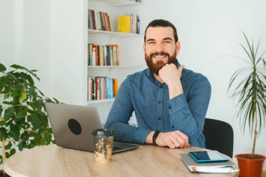Ofisteki yakışıklı sakallı adam kameraya bakıyor.
