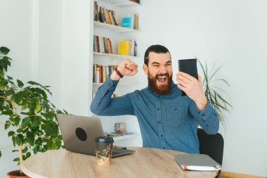 Ofisteki sakallı adam tablete bakıyor ve zaferi kutluyor.