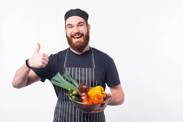 Фото счастливого бородатого шеф-повара в форме, держащего овощи в миске — стоковое фото
