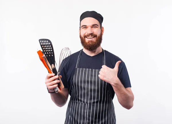 Портрет веселого шеф-повара, держащего в руках посуду и показывающего большой палец — стоковое фото