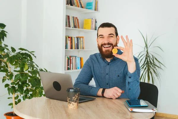 Foto de un hombre alegre con barba en la oficina mostrando Bitcoin —  Fotos de Stock