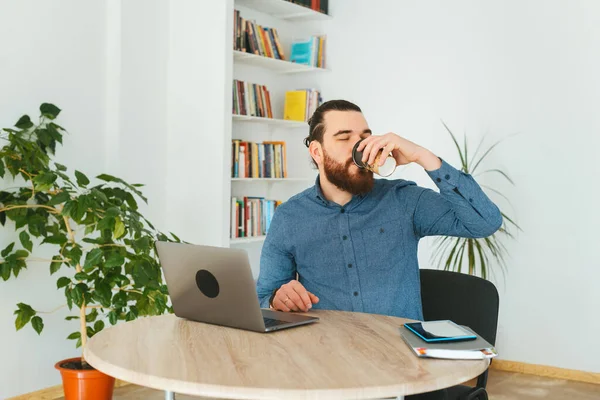 Foto de hombre con barba en la oficina bebiendo taza de café —  Fotos de Stock