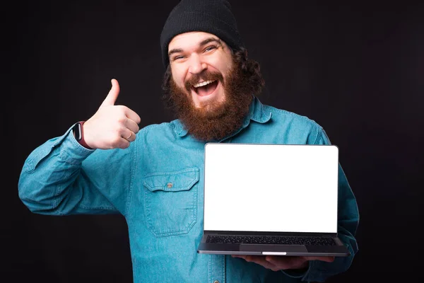 Pria hipster berjenggot ceria muncul ibu jari dan memegang laptop — Stok Foto