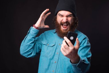 Kızgın sakallı hippi adam akıllı telefondan bağırıyor ve el kol hareketi yapıyor.