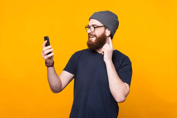 Photo of bearded hipster man looking at smartphone and listening music at earpods — Stock Photo, Image