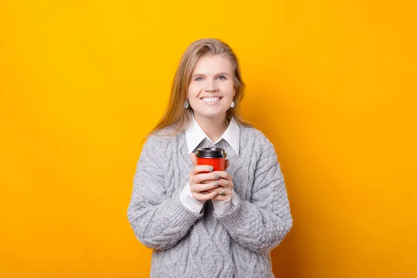 Mujer joven en suéter sosteniendo taza de café sobre fondo amarillo — Foto de Stock