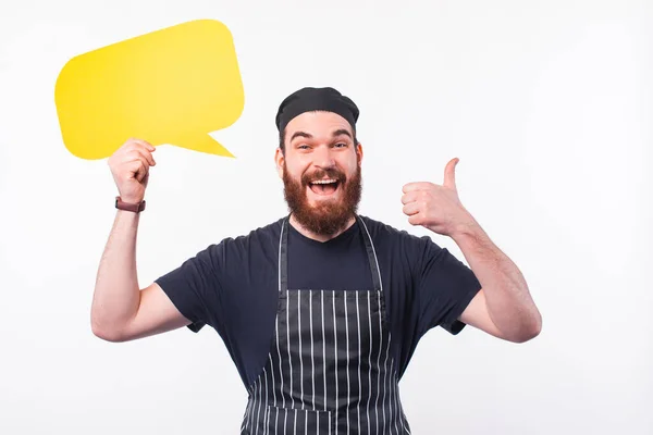 Фото веселого шеф-повара, показывающего большой палец и держащего пустой пузырь речи — стоковое фото