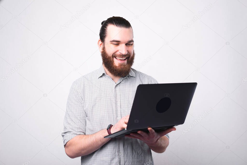 Portrait of happy bearded man in shirt using laptop over white wall