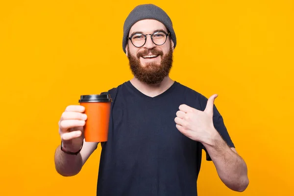 Молодий усміхнений чоловік насолоджується кавою і показує великий палець — стокове фото