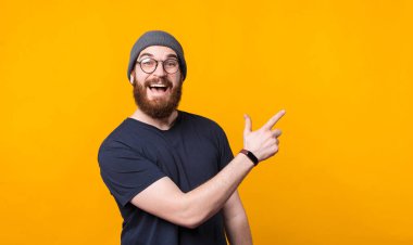 Şaşırmış bir adam boş bir yeri işaret ediyor ve kameraya bakıyor.