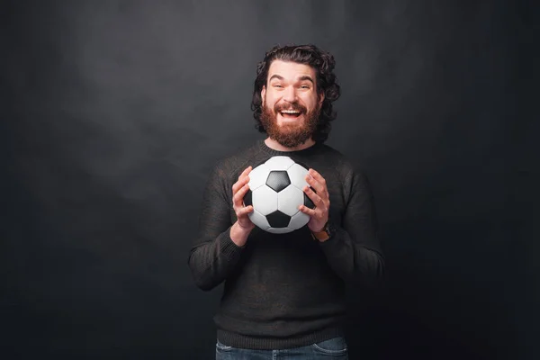 Ein Mann hält aufgeregt einen Fußball in der Nähe einer schwarzen Wand — Stockfoto