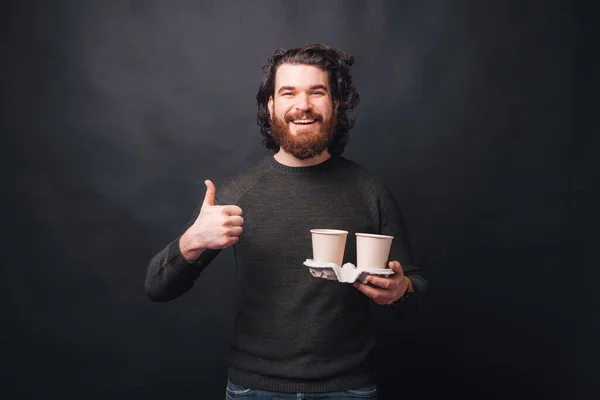 Una foto de un hombre sonriendo a la cámara y sosteniendo dos tazas de bebidas calientes agradeciendo su calidad — Foto de Stock