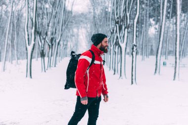 Genç sakallı bir adam kışın ormanda yürüyor.