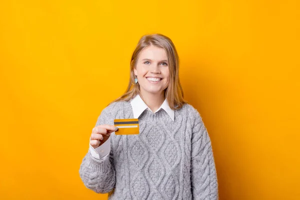 Uma jovem alegre está segurando um cartão de crédito e olhando para a câmera está sorrindo — Fotografia de Stock