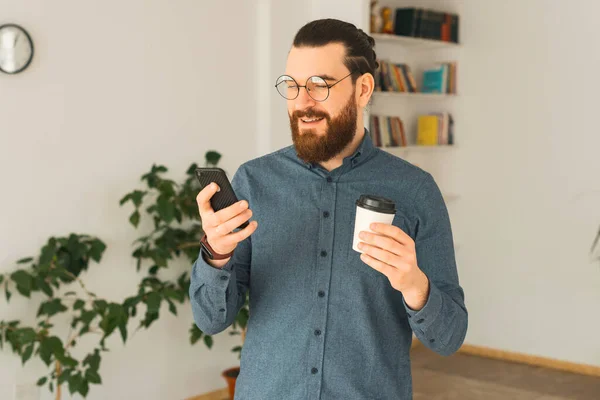 Un jeune hipster barbu au bureau boit du café et parle sur son téléphone — Photo