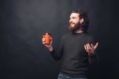 Mutlu genç sakallı adam elinde bir fincan sıcak içecek tutuyor gülümsüyor ve başka tarafa bakıyor.