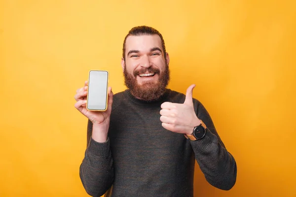 Imagen de un hombre sonriendo a la cámara está sosteniendo un teléfono inteligente y mostrando un pulgar hacia arriba — Foto de Stock