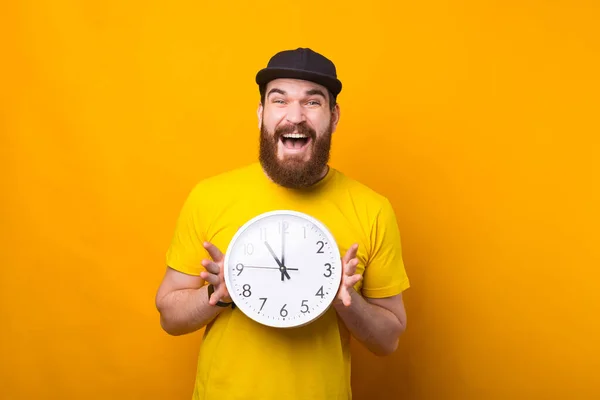 Bild eines aufgeregten Mannes, der lächelnd eine Uhr in der Nähe einer gelben Wand hält — Stockfoto