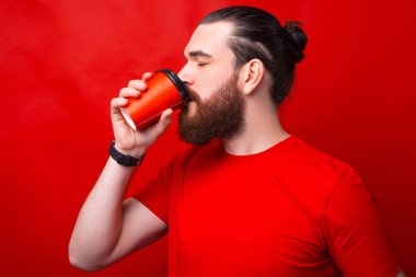 Kırmızı duvarın yanında kahve içen bir adamın fotoğrafı.