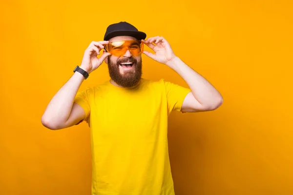 Fénykép vidám szakállas hipster férfi sárga pólóban visel nagy sárga szemüveg és mosolygós — Stock Fotó