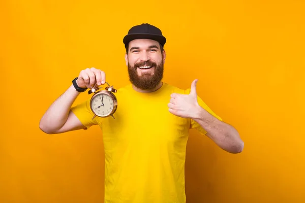 Φωτογραφία του νεαρού hipster άνθρωπος κρατώντας το ξυπνητήρι και δείχνει τον αντίχειρα επάνω, το σχεδιασμό του χρόνου — Φωτογραφία Αρχείου