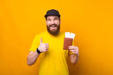 Sakallı yakışıklı genç adam tatile hazır ve elinde biletlerle pasaportu var.
