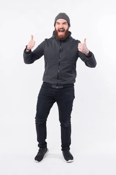 Pełna długość zdjęcie zdumiony brodaty hipster człowiek pokazuje kciuk w górę — Zdjęcie stockowe